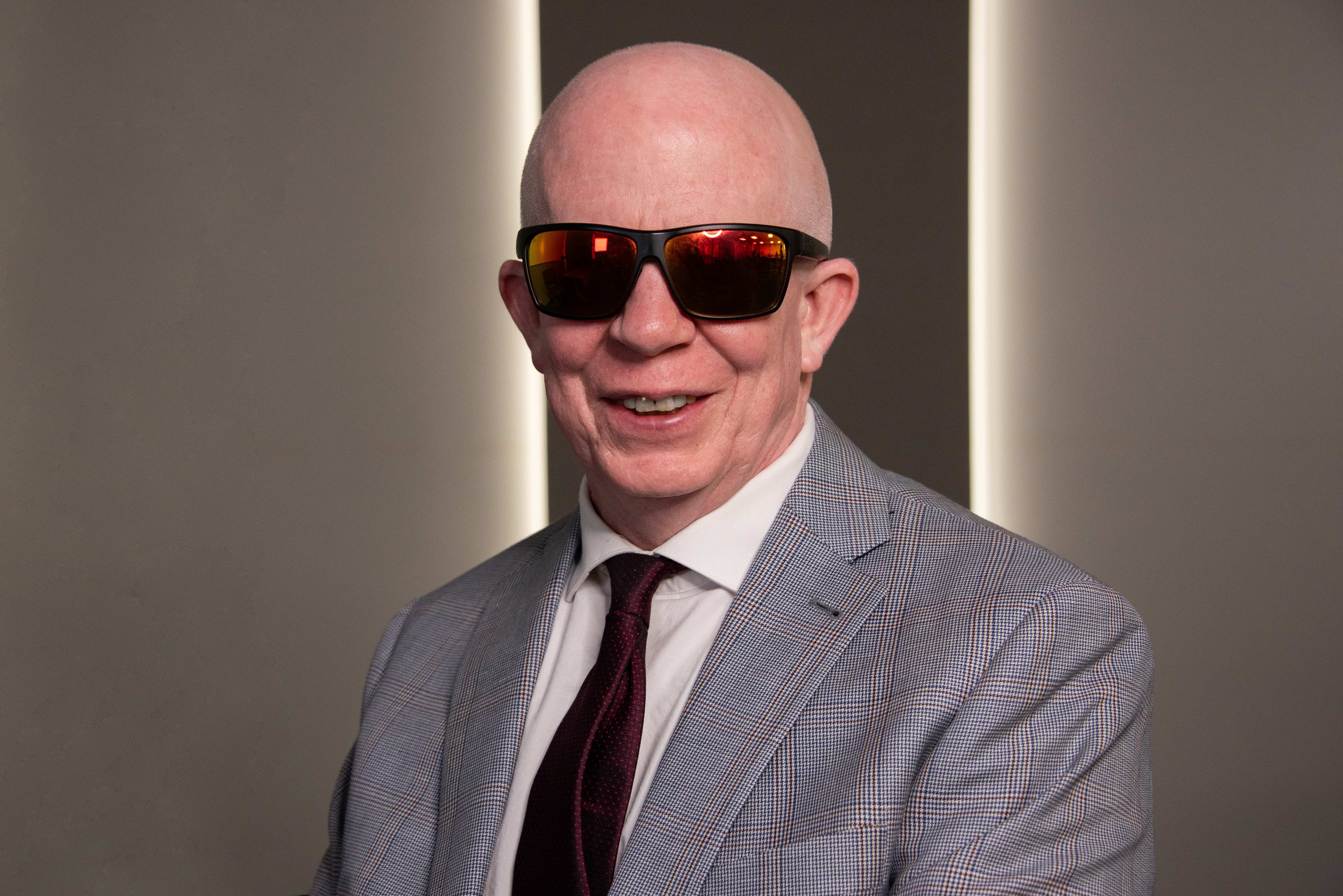 William Black wearing a gray suit and tie and dark glasses.